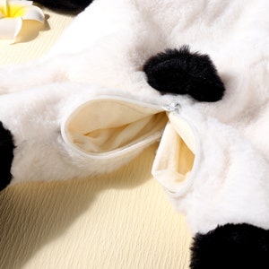 May include: Close-up of a white and black plush panda bear costume with a zippered pocket. The costume has black accents and a soft, furry texture. The pocket is beige and has a silver zipper.