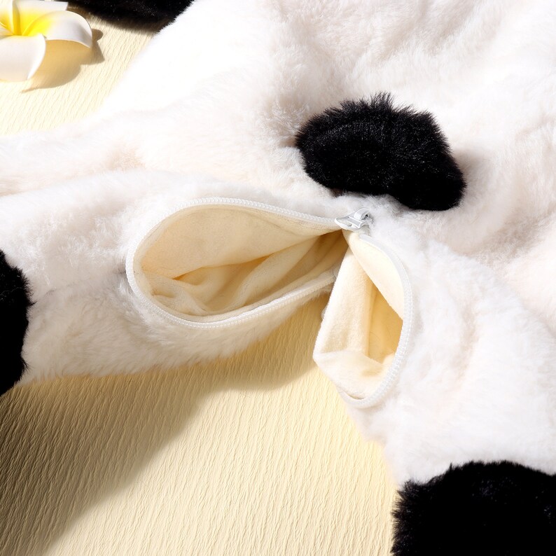 May include: Close-up of a white and black plush panda bear costume with a zippered pocket. The costume has black accents and a soft, furry texture. The pocket is beige and has a silver zipper.