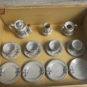 May include: A miniature porcelain tea set housed in a wooden display box with a glass lid. The set includes a teapot, a creamer, a sugar bowl, four teacups with matching saucers, and four additional saucers, all featuring a delicate blue and red floral pattern.