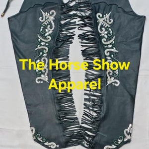 May include: Black leather chaps with fringe and green and white embroidery. The chaps have the text "The Horse Show Apparel" on them.