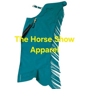 Op de afbeelding: Turquoise suède chaps met franjes en een rits aan de zijkant. Het logo van The Horse Show Apparel is op de voorkant gedrukt.