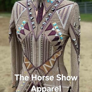 May include: A beige show jacket with a geometric design featuring brown, purple, and silver accents. The jacket is embellished with rhinestones and has a zipper closure. The text "The Horse Show Apparel" is printed on the front of the jacket.