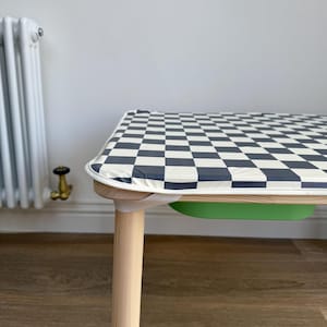 May include: A wooden children's table with a black and white checkered tablecloth. The table has a green tray underneath the tabletop.