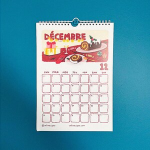 Op de afbeelding: Een decemberkalender met een feestelijke illustratie. De bovenkant toont het woord "D&Eacute;CEMBRE" en een vakantiesc&egrave;ne met cadeaus en desserts. Het kalenderraster is rood met data en dagen van de week.