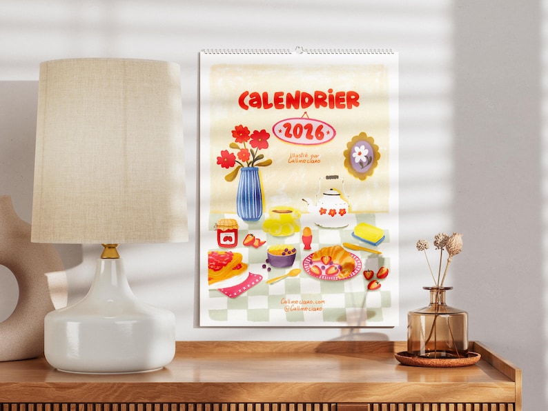 Op de afbeelding: Een kalender voor 2026 met een grillige illustratie van een ontbijt, met een vaas met rode bloemen, een theepot en diverse etenswaren. Het woord "CALENDRIER" staat bovenaan.