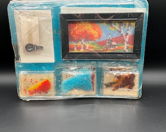 May include: A craft kit with a framed picture of a fall scene with a red, orange, and yellow tree. The kit includes three bags of colorful beads.