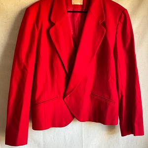 Puede incluir: Una chaqueta roja brillante con un cierre de botón único y un dobladillo ligeramente asimétrico.