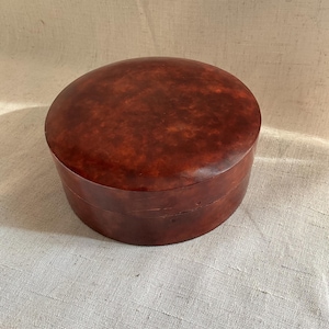 Puede incluir: Una caja redonda de madera con un acabado marrón oscuro moteado. La caja tiene una tapa y está hecha de un material natural.