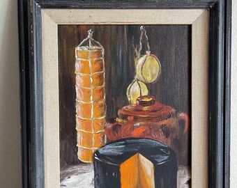 May include: Oil painting of a still life featuring a wheel of cheese with a wedge cut out, a sausage, and a teapot. The painting is in a black frame with a linen mat.