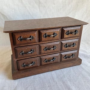 May include: A wooden jewelry box with eight drawers and black metal handles. The box is made of dark wood and has a simple design.