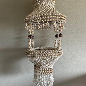 Könnte beinhalten: Ein weißer Muschel-Kronleuchter mit einem Drahtgestell und braunen Muscheln, die von unten hängen. Der Kronleuchter besteht aus vielen kleinen Muscheln und hat einen einzigartigen, böhmischen Stil.