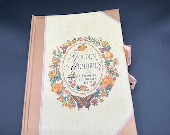 May include: A vintage photograph album with the words "Golden Memories" and "A Victorian Photograph Album" on the cover. The cover features a floral and butterfly design in shades of yellow, orange, and pink. The album has a pink ribbon tie.