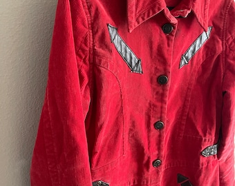 May include: A long red corduroy jacket with black leather accents and button closures. The jacket has a pointed collar and a  "ESSENTIALLY GIRLS" label.