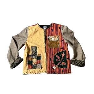 Könnte beinhalten: Eine Patchwork-Jacke mit einzigartigem Design. Die Jacke hat eine Kombination aus beigen, orangefarbenen und braunen Stoffen. Die Ärmel sind gesprenkelt grau und die Manschetten haben ein geometrisches Muster. Die Jacke hat einen Knopfverschluss und dekorative Aufnäher.