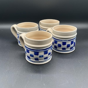 May include: Set of four ceramic mugs with a blue and white checkered pattern. The mugs have a light gray base and a white rim.