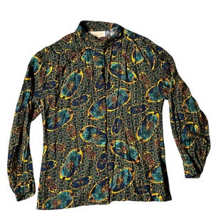 May include: A long-sleeved blouse with a high collar. The dark green fabric is patterned with teal, gold, and maroon oval shapes, set against a geometric background. The blouse has pleats down the front and gathered sleeves.