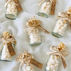 Peut inclure: Petites bouteilles en verre remplies de bonbons blancs en forme de c&oelig;ur, orn&eacute;es de fleurs s&eacute;ch&eacute;es, de dentelle et de ficelle. Chaque bouteille a une petite &eacute;tiquette avec du texte. Une charmante faveur de mariage.