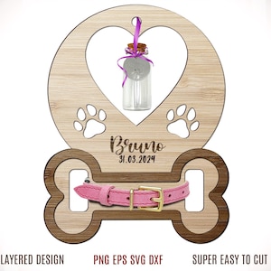 May include: A wooden pet memorial with a heart-shaped top, paw prints, and a bone-shaped bottom. It features a small glass bottle, a pink collar, and the name "Bruno" with the date 31.03.2024. The design is layered.