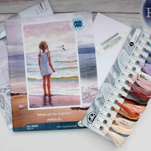 May include: A cross-stitch kit featuring a girl standing on a beach with the words "Where are the dolphins?" and "Crafts for Fun" printed on the front. The kit includes a colour chart with DMC floss colours and a printed pattern.