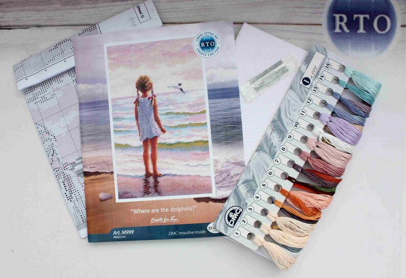 May include: A cross-stitch kit featuring a girl standing on a beach with the words "Where are the dolphins?" and "Crafts for Fun" printed on the front. The kit includes a colour chart with DMC floss colours and a printed pattern.