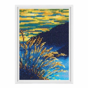 Puede incluir: Una bordadura de punto de cruz enmarcada que representa una puesta de sol sobre una masa de agua con hierba alta en primer plano. El cielo es un degradado de amarillo, naranja y azul, mientras que el agua es de un azul profundo. La hierba es una mezcla de marrón y verde.