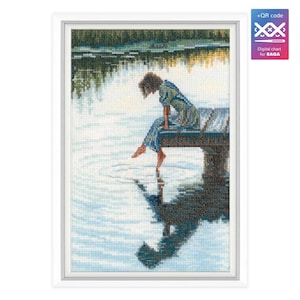 May include: A cross-stitch pattern featuring a woman sitting on a wooden dock over a lake. The woman is wearing a blue dress and has her feet in the water. The water is a light blue color and there are ripples in the water.
