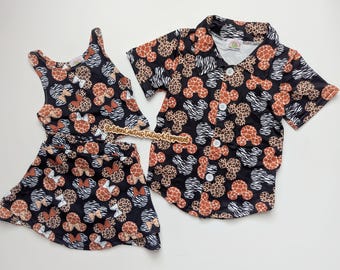 May include: A black outfit set featuring a tank top and skirt, and a button-down shirt. The set is patterned with Mickey Mouse silhouettes, giraffe print, and zebra stripes. The outfit is designed for children.