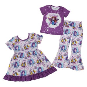 May include: A purple short-sleeved t-shirt, a dress, and flared pants. The t-shirt has a graphic with the word "HUNTRA". The dress and pants are patterned with a cartoon character. The dress has a ruffled hem. The outfits are for children.