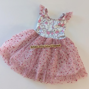 May include: A pink tutu dress with a bodice featuring a cat print. The dress has a layered tulle skirt with scattered pink sequins. The straps have small tulle accents. The text "Golden Cactus Tutus & Apparel" is visible.