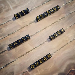 May include: Four necklaces with black beads spelling out the words "BEST", "FRIENDS", "CHILL", and "QUEEN" in gold lettering.