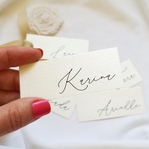 May include: White place cards with names written in black calligraphy. The names are "Karina", "Anelle", and "Leni".