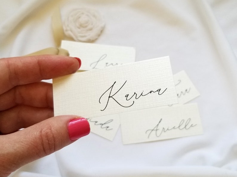 May include: White place cards with names written in black calligraphy. The names are "Karina", "Anelle", and "Leni".