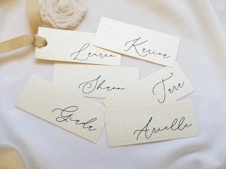 May include: Six white place cards with black calligraphy names: Giada, Lauren, Kerri, Shana, Tara, and Arielle.