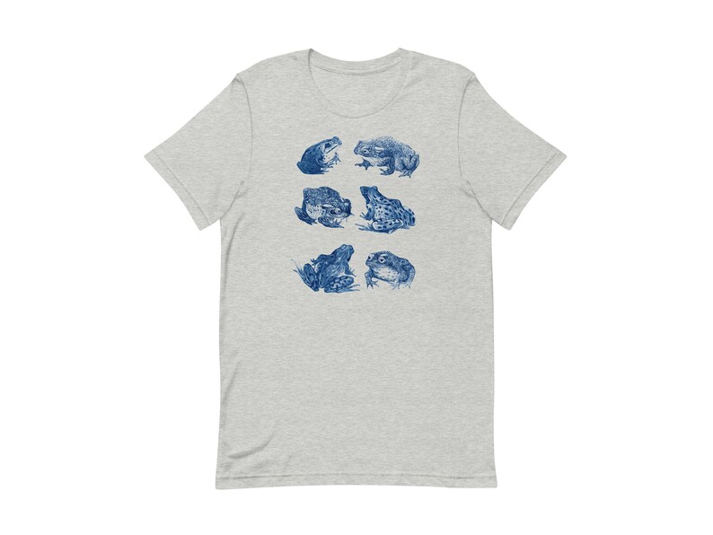 K&ouml;nnte beinhalten: Ein hellgraues T-Shirt mit einem blauen Aufdruck von verschiedenen Fr&ouml;schen in verschiedenen Posen.