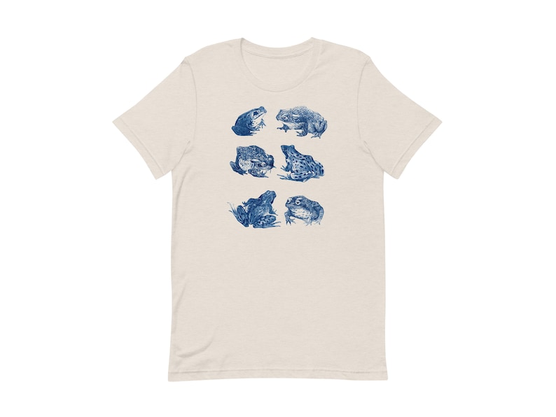 K&ouml;nnte beinhalten: Ein hellbeiges T-Shirt mit einem blauen Aufdruck von sechs Fr&ouml;schen in verschiedenen Posen.