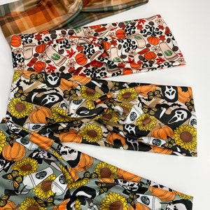 May include: Four fabric headbands with twisted knot designs. The headbands feature fall-themed patterns, including plaid, pumpkins, coffee cups, sunflowers, ghosts, and butterflies. The colors include orange, brown, green, black, and yellow.