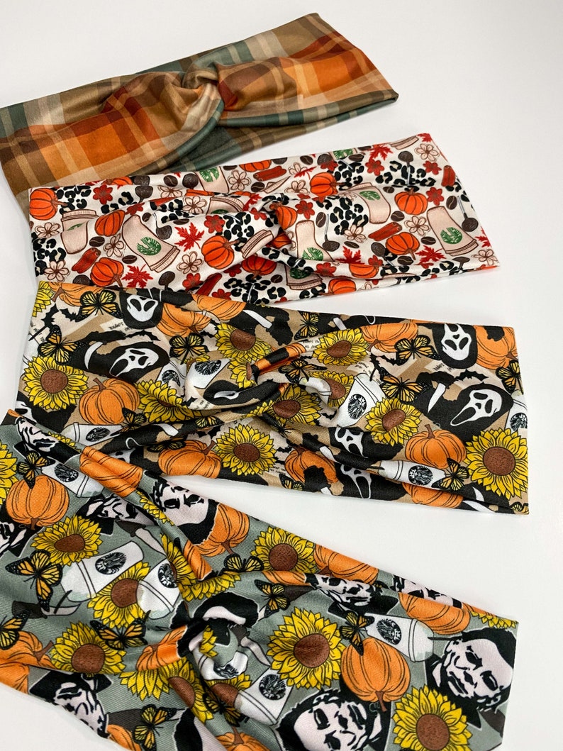 May include: Four fabric headbands with twisted knot designs. The headbands feature fall-themed patterns, including plaid, pumpkins, coffee cups, sunflowers, ghosts, and butterflies. The colors include orange, brown, green, black, and yellow.