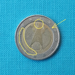 May include: A silver German 1 Euro coin with a gold eagle design. The eagle has a spread wingspan and is facing right. The coin has the year 2002 inscribed on the bottom.