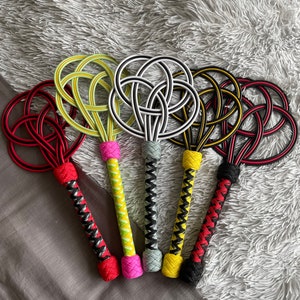 Puede incluir: Cinco látigos coloridos con mangos de diferentes colores y diseños de cuerda trenzada. Los látigos tienen una forma circular en el extremo y están hechos de cuerda negra, roja, amarilla, verde y blanca.