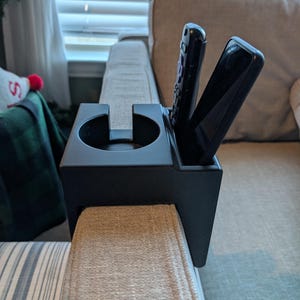 May include: Black plastic couch armrest caddy with a cup holder and two slots for remotes.