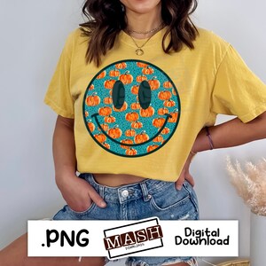 May include: Mustard yellow t-shirt featuring a large smiley face design filled with orange pumpkins on a teal background. The smiley face has black eyes and a curved black mouth. The shirt is a digital download.