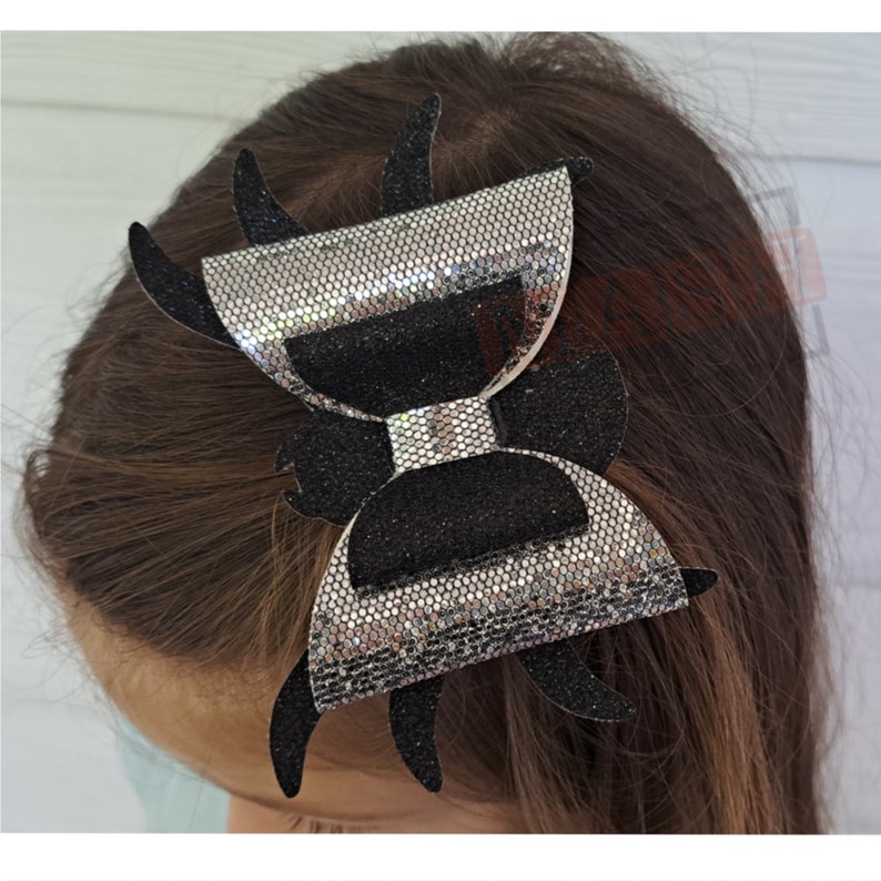 May include: A black and silver glitter spider bow hair clip. The bow is shaped like a spider with eight legs.