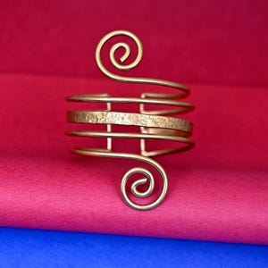 May include: A gold-toned metal bracelet with a spiral design on each end. The bracelet is made of multiple bands of metal.