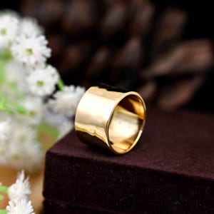 Puede incluir: Un anillo de banda ancha de oro con un acabado martillado. El anillo es grueso y tiene un borde redondeado.