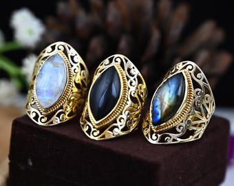 May include: Three gold rings with ornate filigree designs. The rings feature different gemstone insets: a white moonstone, a black stone, and a blue labradorite.