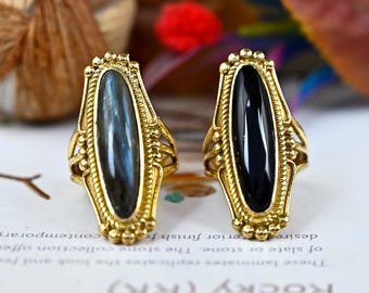 May include: Two gold rings with oval-shaped stones. The ring on the left has a dark blue stone, and the ring on the right has a black stone.