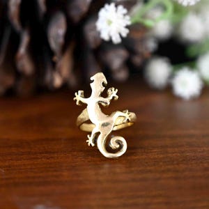 May include: A gold-toned ring featuring a detailed gecko design. The ring is made of metal and has a smooth finish.