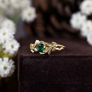 Puede incluir: Un anillo de oro con una piedra preciosa verde engastada en un diseño de hojas.