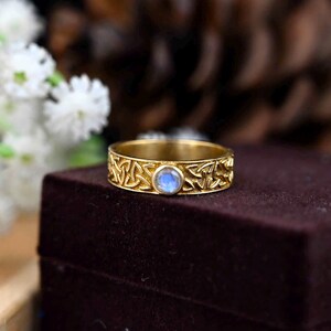 May include: A gold ring featuring a Celtic knot design and a blue moonstone at its centre.