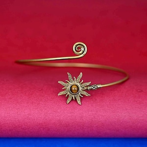 May include: A gold-toned bangle bracelet with a sun-shaped charm featuring a tiger's eye stone in the center.